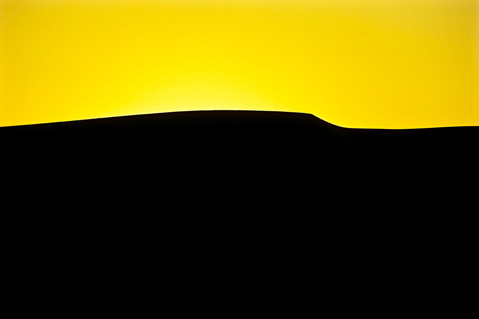 The silhouette of a vast sand dune crest against a vivid yellow sky. near Sossusvlei, Great Southern Dune Field, Namib-Naukluft National Park, Namibia.