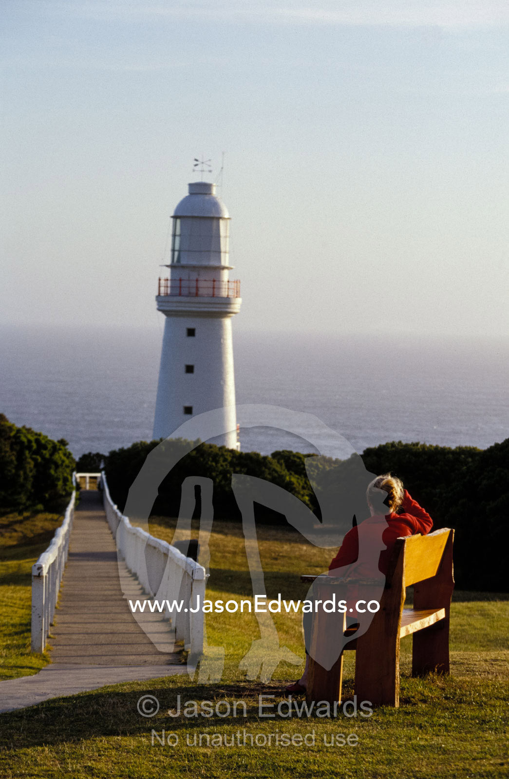 A tourist watching the sunset over a lighthouse and ocean. Cape Otway National Park, Victoria, Australia.