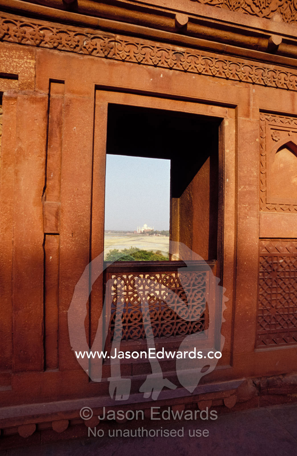 An Agra Fort carved sandstone window, framing the distant Taj Mahal. Agra, India.