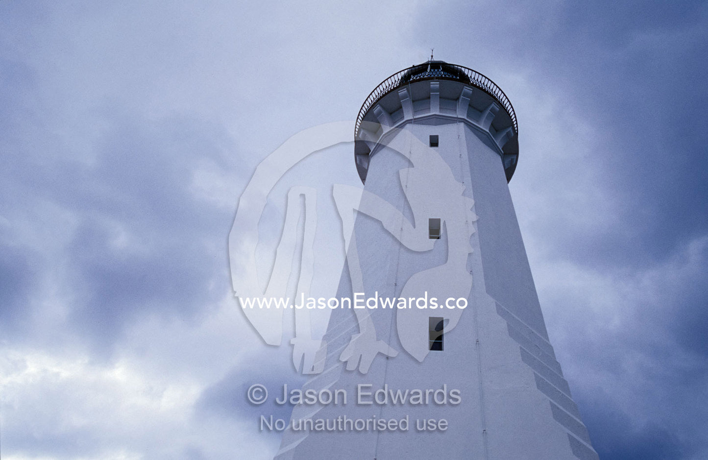 Looking up at a white antique lighthouse with storm clouds behind. Green Cape, Ben Boyd National Park, New South Wales, Australia.