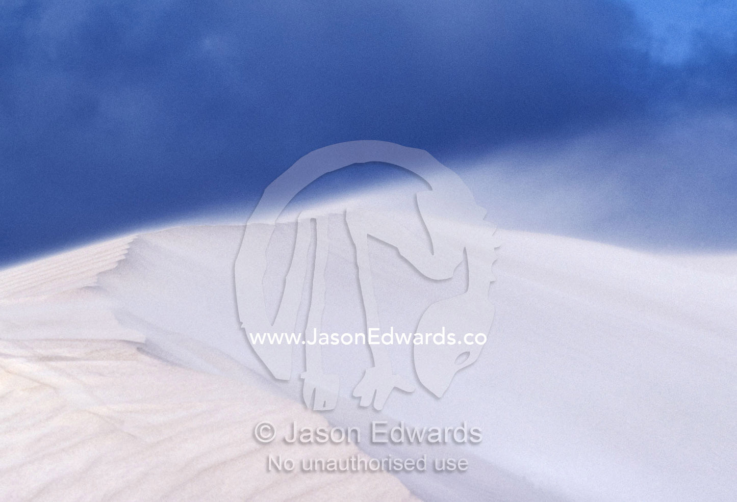 Winds blast across the peak of a white sand dune, wisping away sand. near Cactus Beach, South Australia.