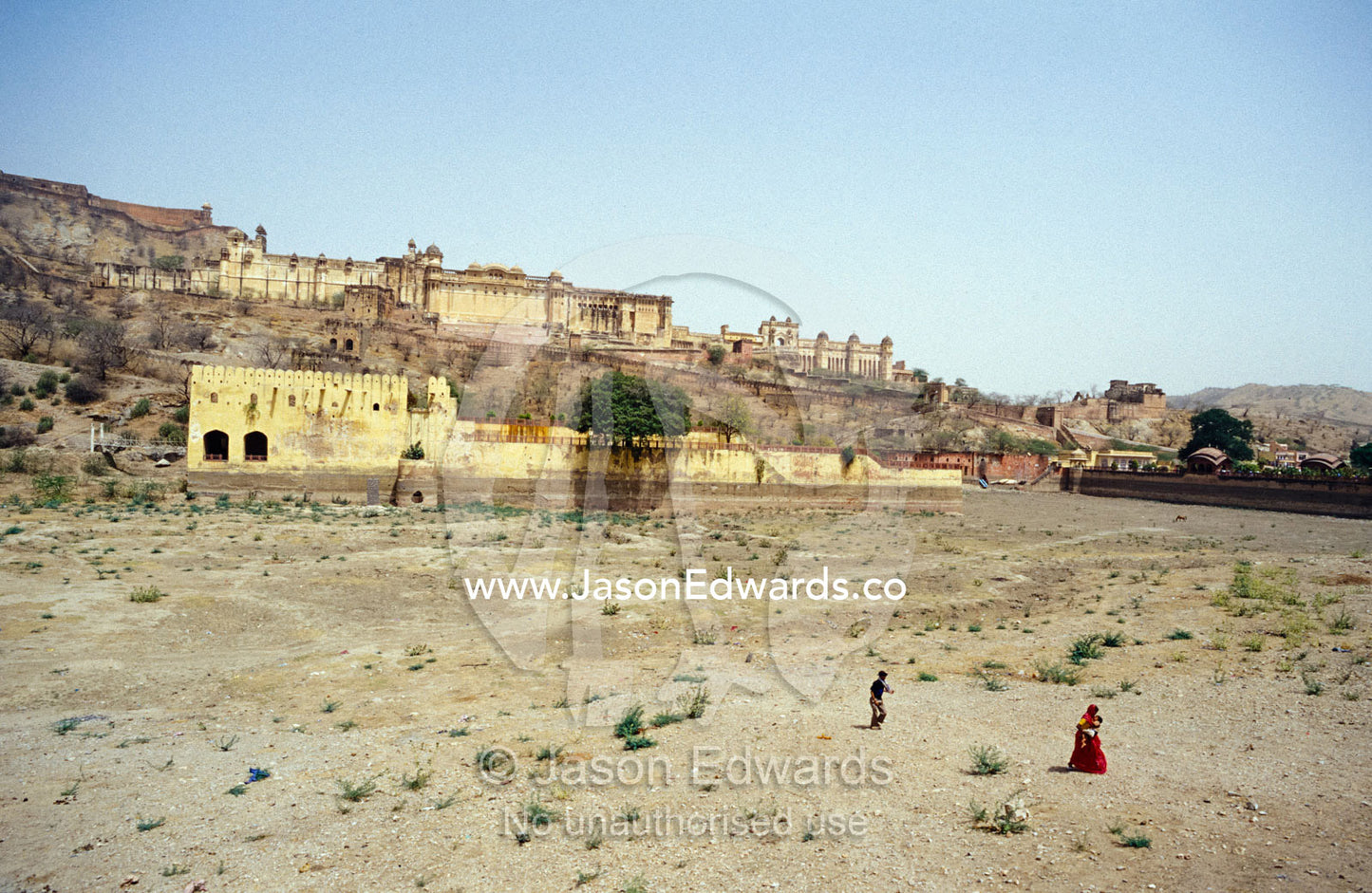 A woman with a baby and child crosses a dry lake bed in drought. Amber Fort Jaipur, India