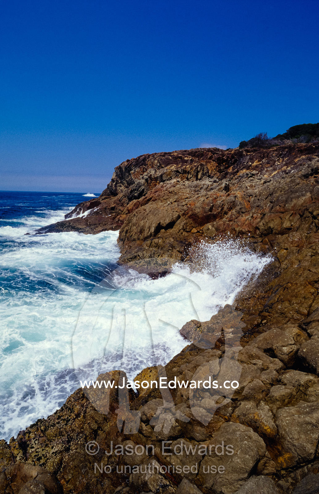Ocean waves pound against the ruggered rocky coast. Tathra, New South Wales, Australia.