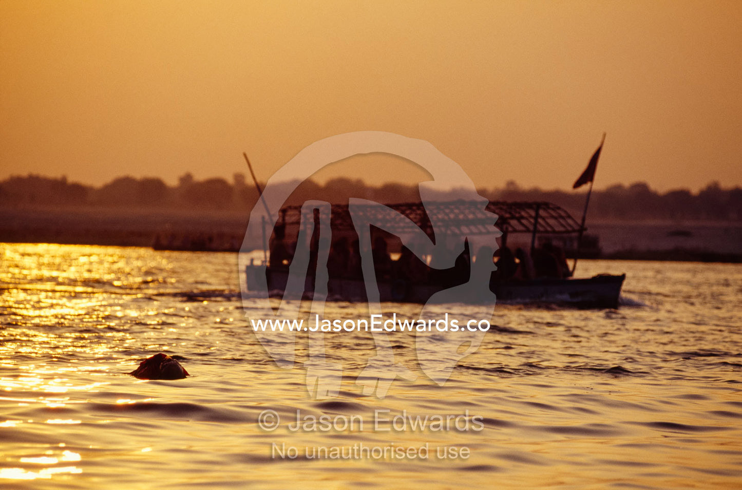 A water tazi motors past a sadu's body in the Ganges River at dawn. Varanasi (Benares), India.