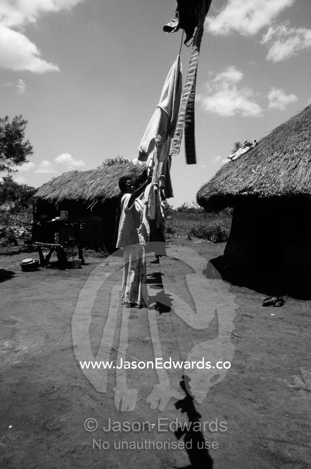 A young African mother hangs out her laundry to dry in her village. Tororo District, Uganda.