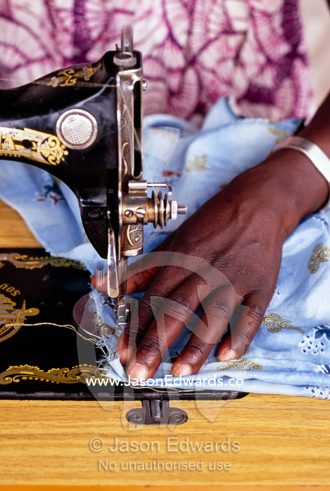 The hands of a seamstress work an antique sewing machine in Uganda. Tororo District, Uganda.