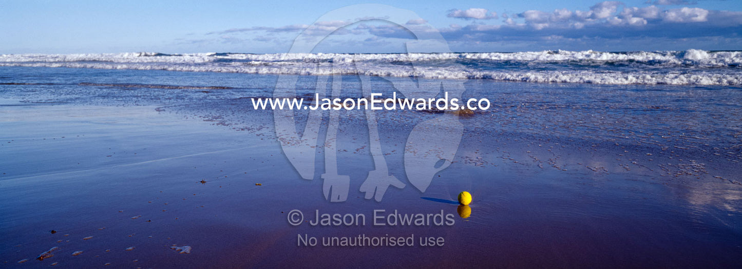 A tennis ball on a wide beach awaits waves to carry it out to sea. Jan Juc, Victoria, Australia.