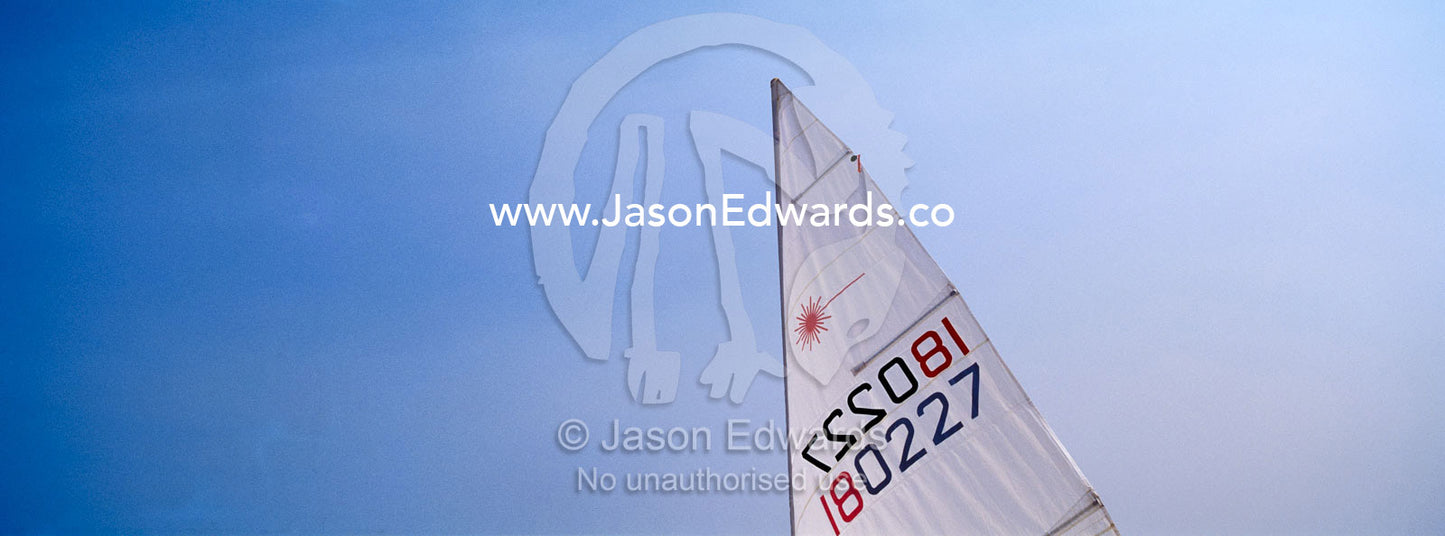 A small yacht sail knifes through a clear blue summer sky. Port Melbourne, Victoria, Australia.