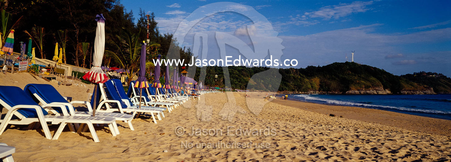 Empty lounges along a tropical island beach at sunset. Rawai Beach, Phuket, Thailand.