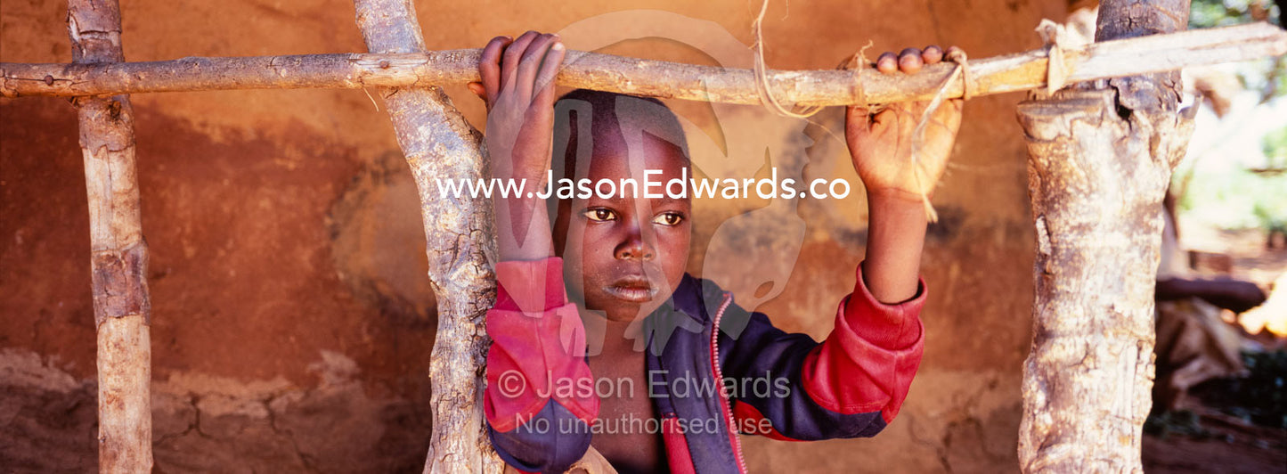 The intense stare of a boy resting from the heat by a village hut. Tororo District, Uganda.