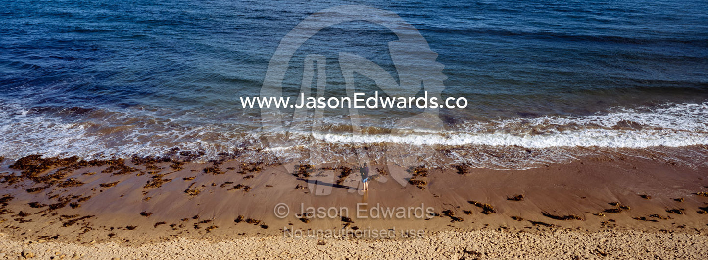 An aerial view of a lone man fishing in the ocean from the beach. Jan Juc, Victoria, Australia.
