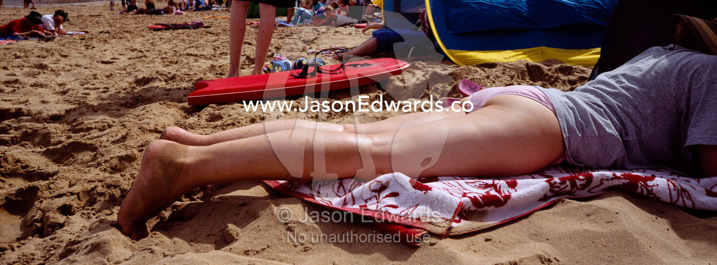 The long elegant legs of a woman sun bathing on a beach during summer. Torquay, Victoria, Australia.
