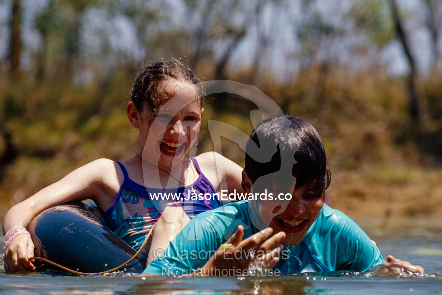 Two sisters play in an outback billabong on a scorching hot day. Limmen National Park, Northern Territory, Australia.