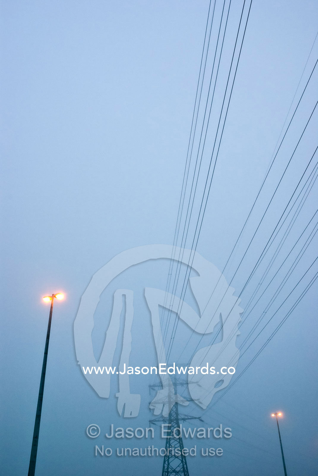 Electricity tower, power cables and freeway lights on a foggy morning. Point Cook, Victoria, Australia.