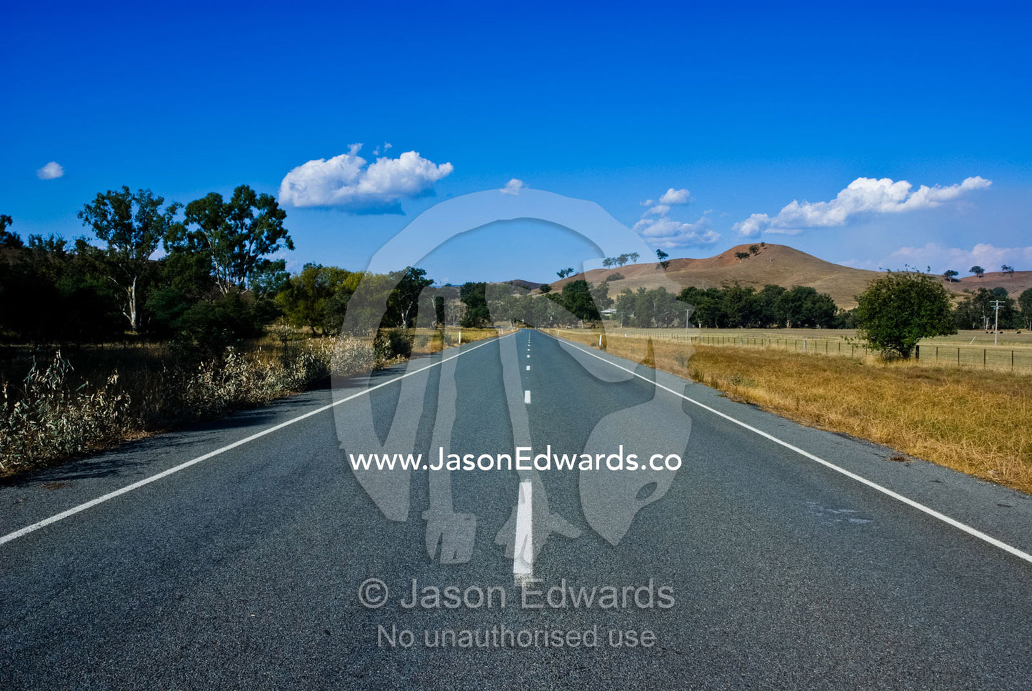 An empty country road passes through farmland and rolling hills. near Yea, Victoria, Australia.