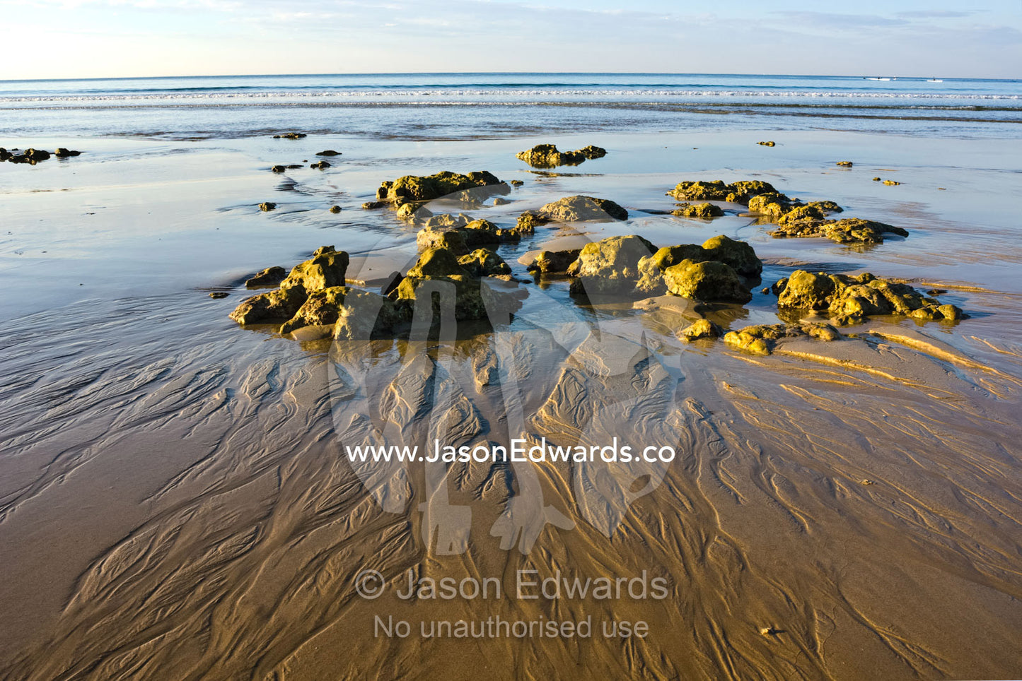 The receding tide leaves patterns in the sand around small boulders. Point Danger, Torquay, Victoria, Australia.