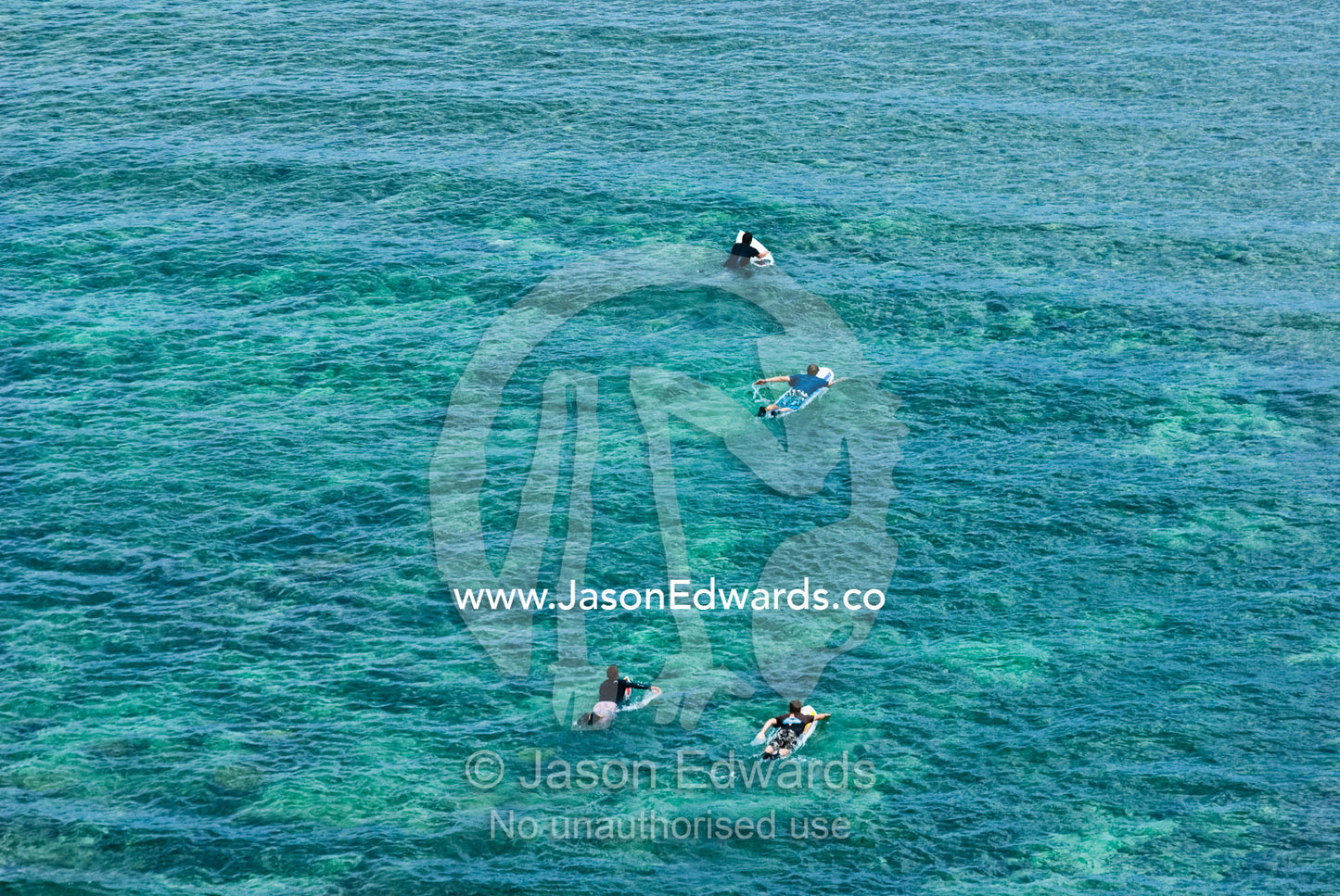 An aerial view of surfers paddling over a reef to catch some waves. Bukit Peninsula, Bali, Indonesia.
