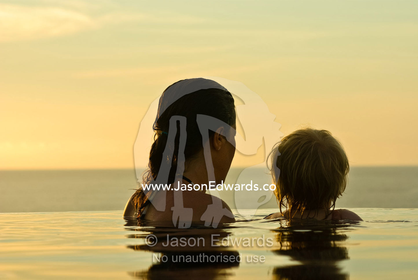 A mother and son watch the sunset from a horizon pool in a villa. The Temple Lodge, Bukit Peninsula, Bali, Indonesia.