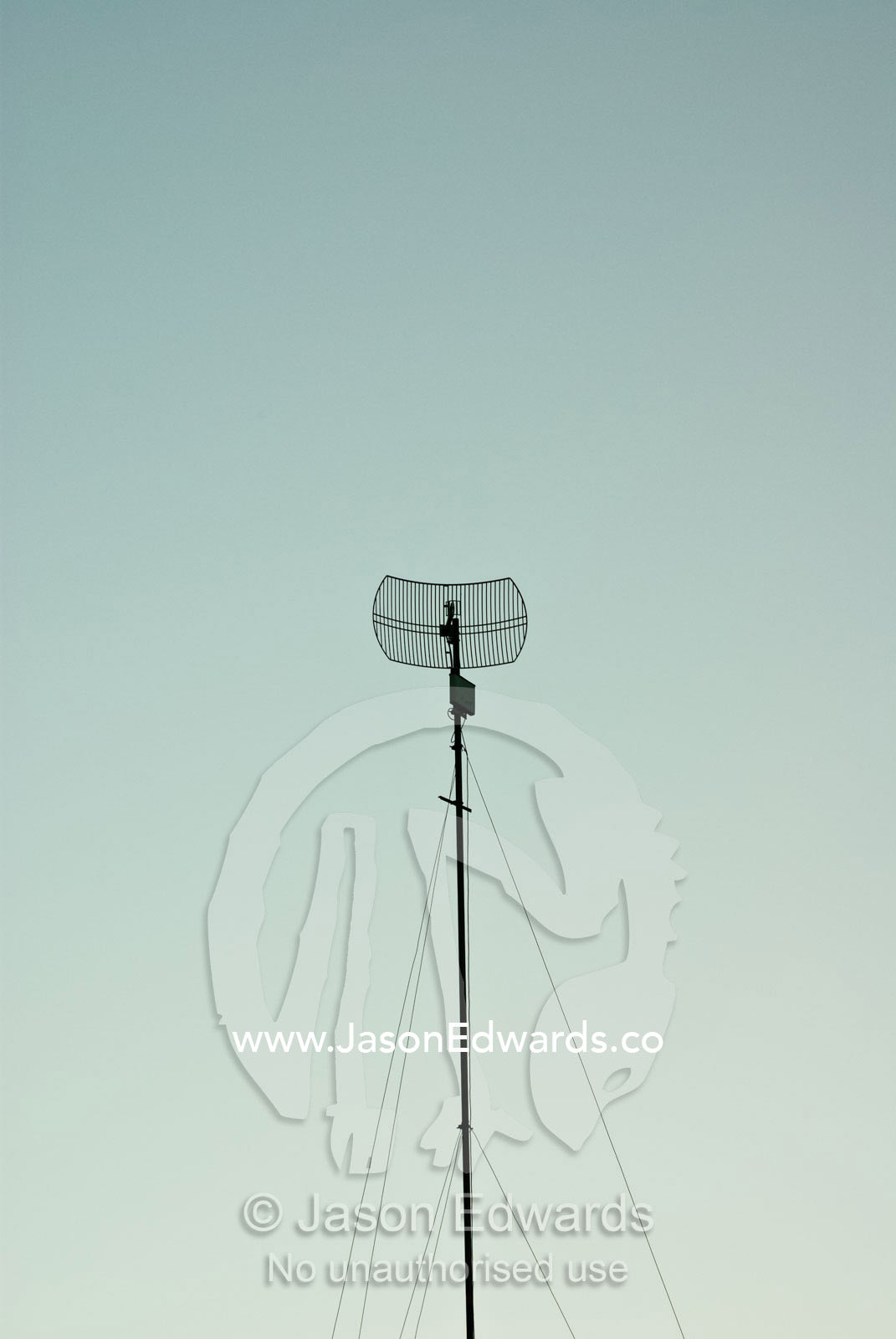 A satellite dish and radio antenna in a clear pastel sky after sunset. Bukit, Bali, Indonesia.
