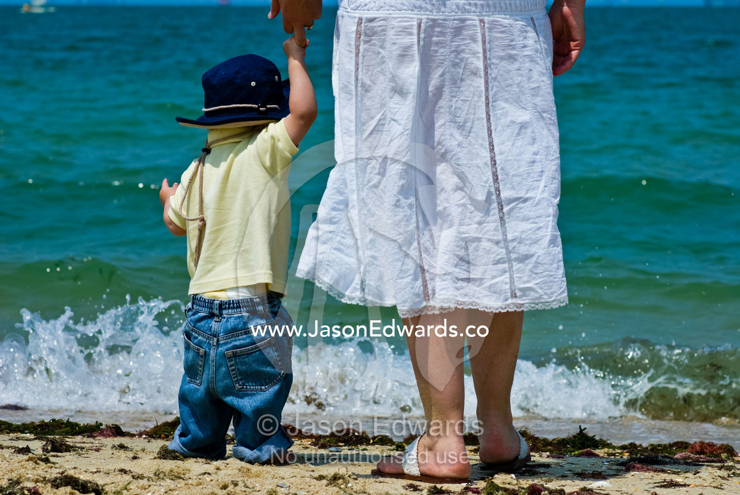A mother holds her sons hand whilst exploring the beach and waves. Port Melbourne, Melbourne, Victoria, Australia.