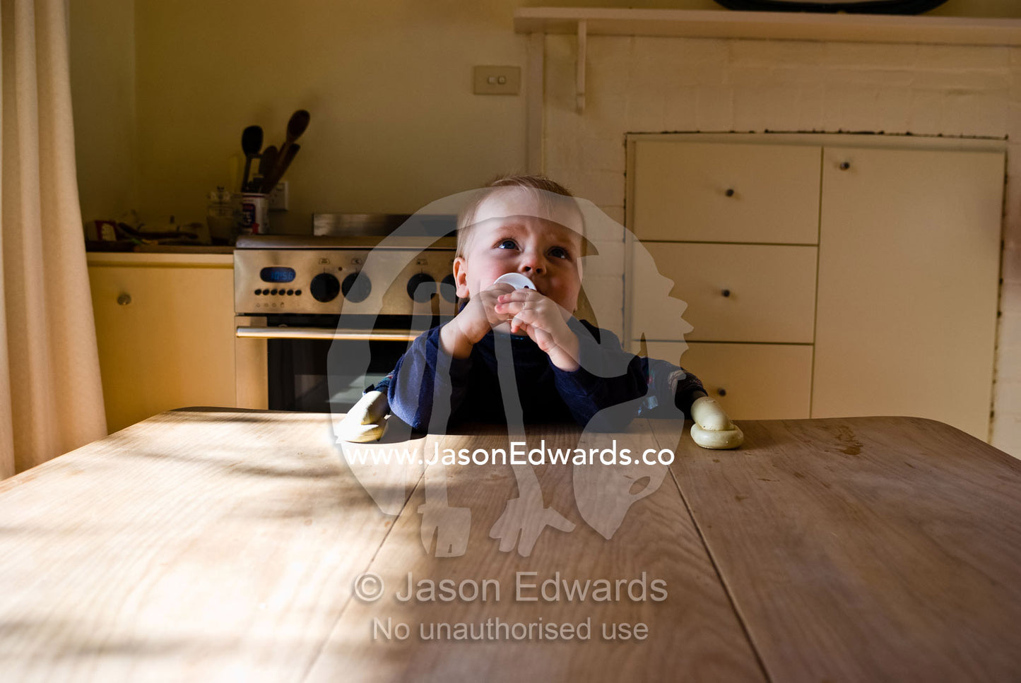 A baby chews on a teething ring whilst sitting at a dining table. Castlemaine, Victoria, Australia.