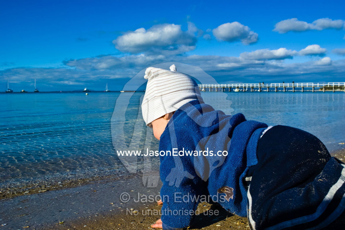 A baby crawls across the sand towards the sea on a sunny winter day. Portsea, Victoria, Australia.