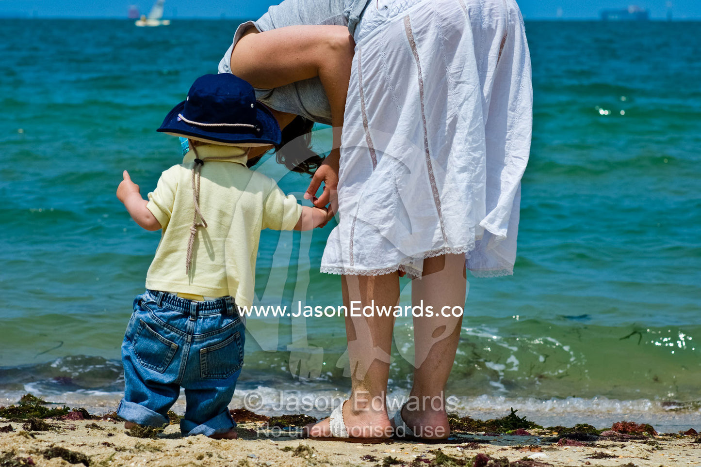 A mother gently kisses her son whilst exploring the beach and waves. Port Melbourne, Victoria, Australia.