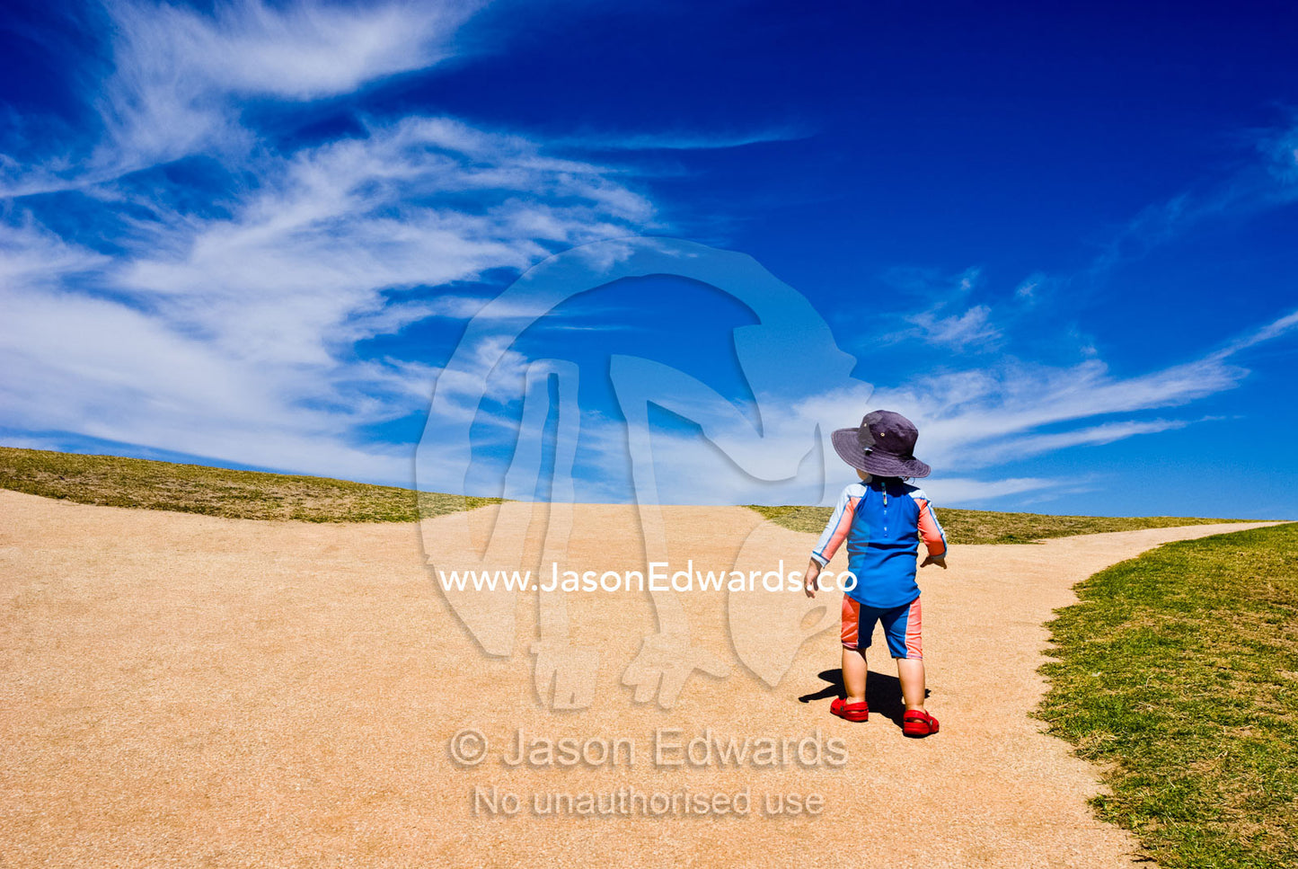 A baby climbs a steep hill towards a blue sky and new horizons. Torquay Point, Torquay, Surf Coast, Victoria, Australia.