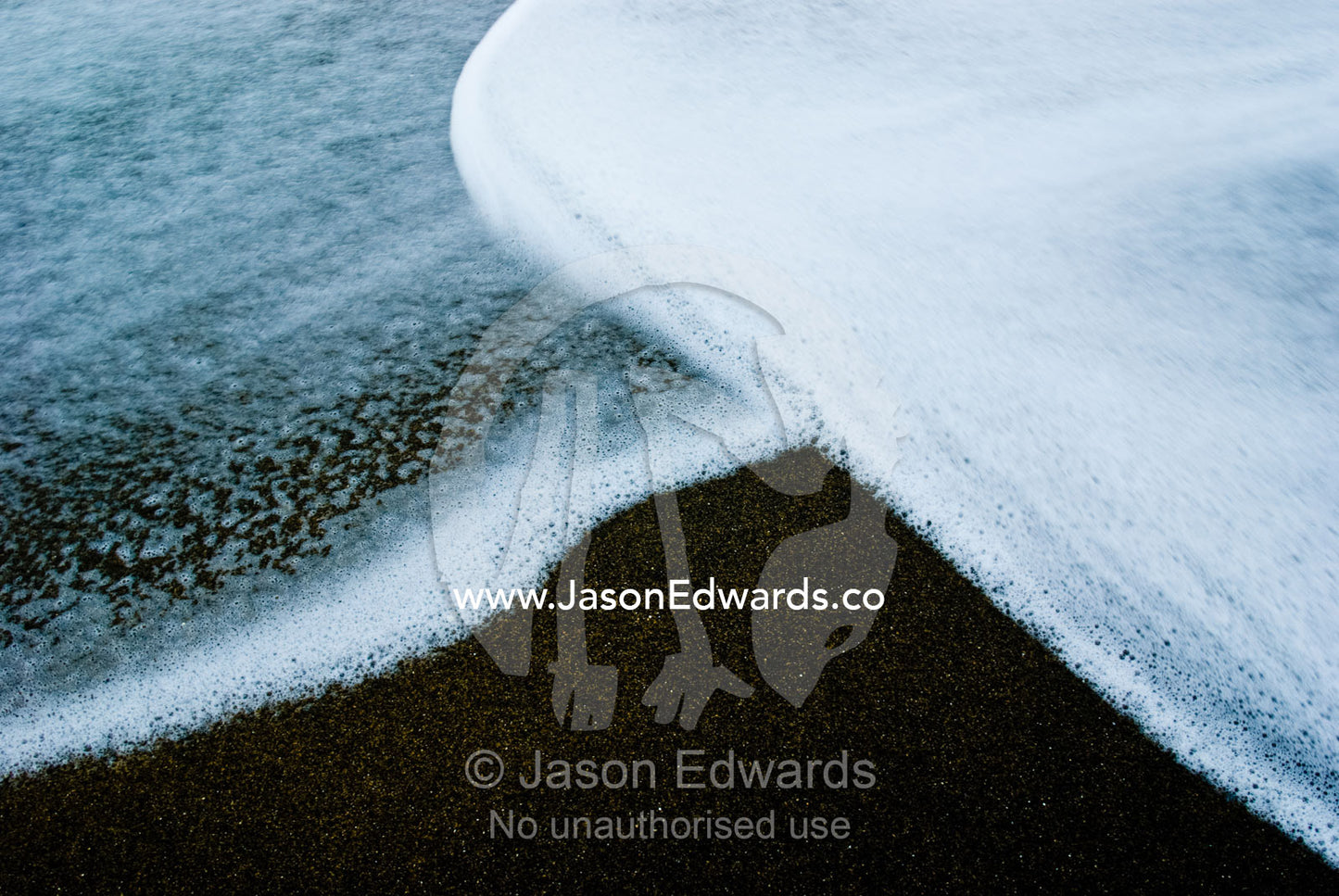 The foamy edges of winter waves overlap on a black sandy beach. Bells Beach Surfing Recreation Reserve, Surf Coast, Victoria, Australia.