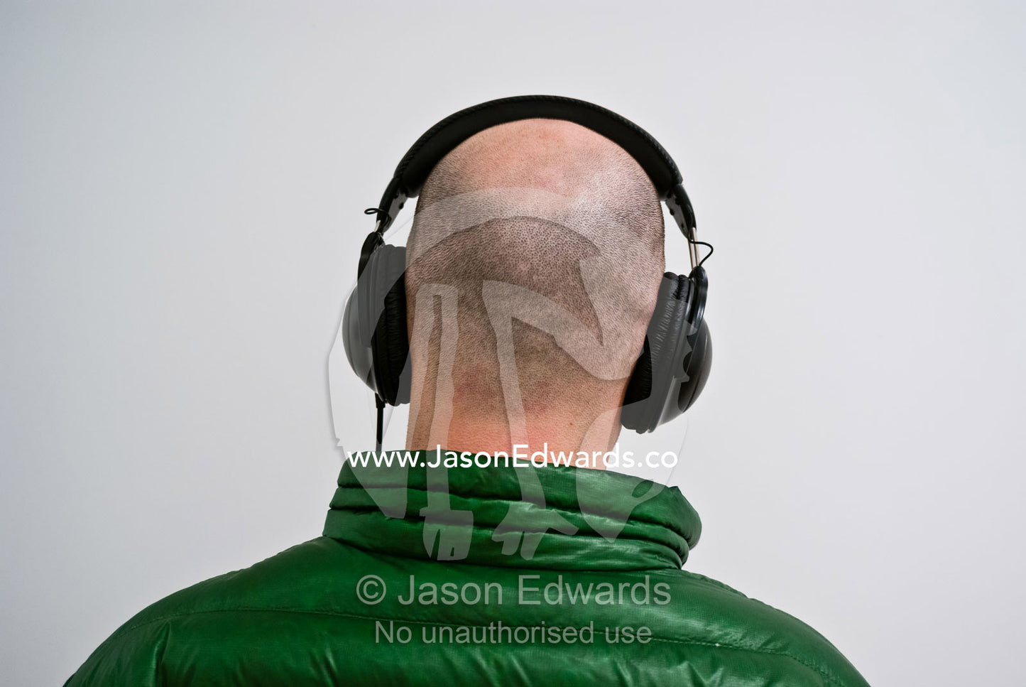 A funky guy in a green winter coat listens to music via headphones. Washington, District of Columbia.