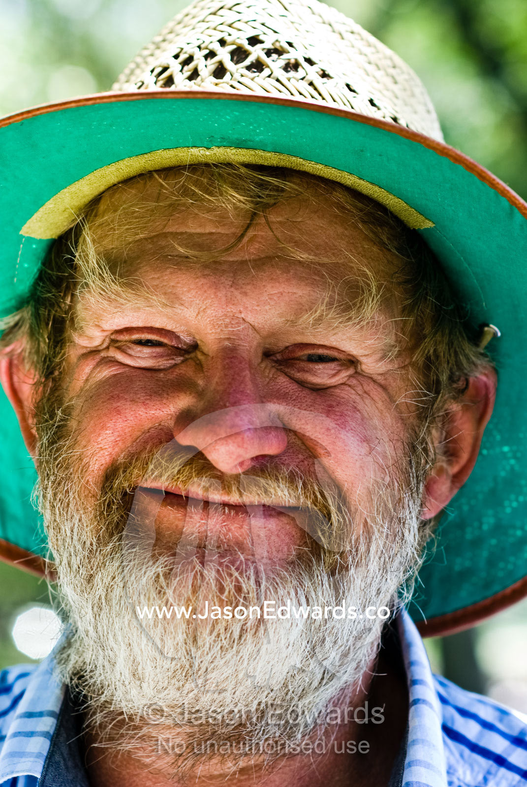 A grizzled chicken farmer in his summer hat smiles at the camera. Yarra River, Melbourne, Victoria, Australia.