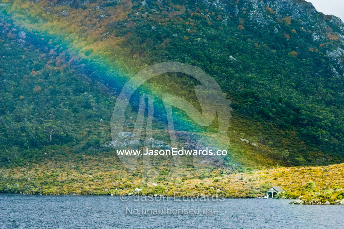 A rainbow descends onto an alpine lake touching an antique boathouse. Dove Lake, Cradle mountain Lake St Clair National Park, Tasmania, Australia.