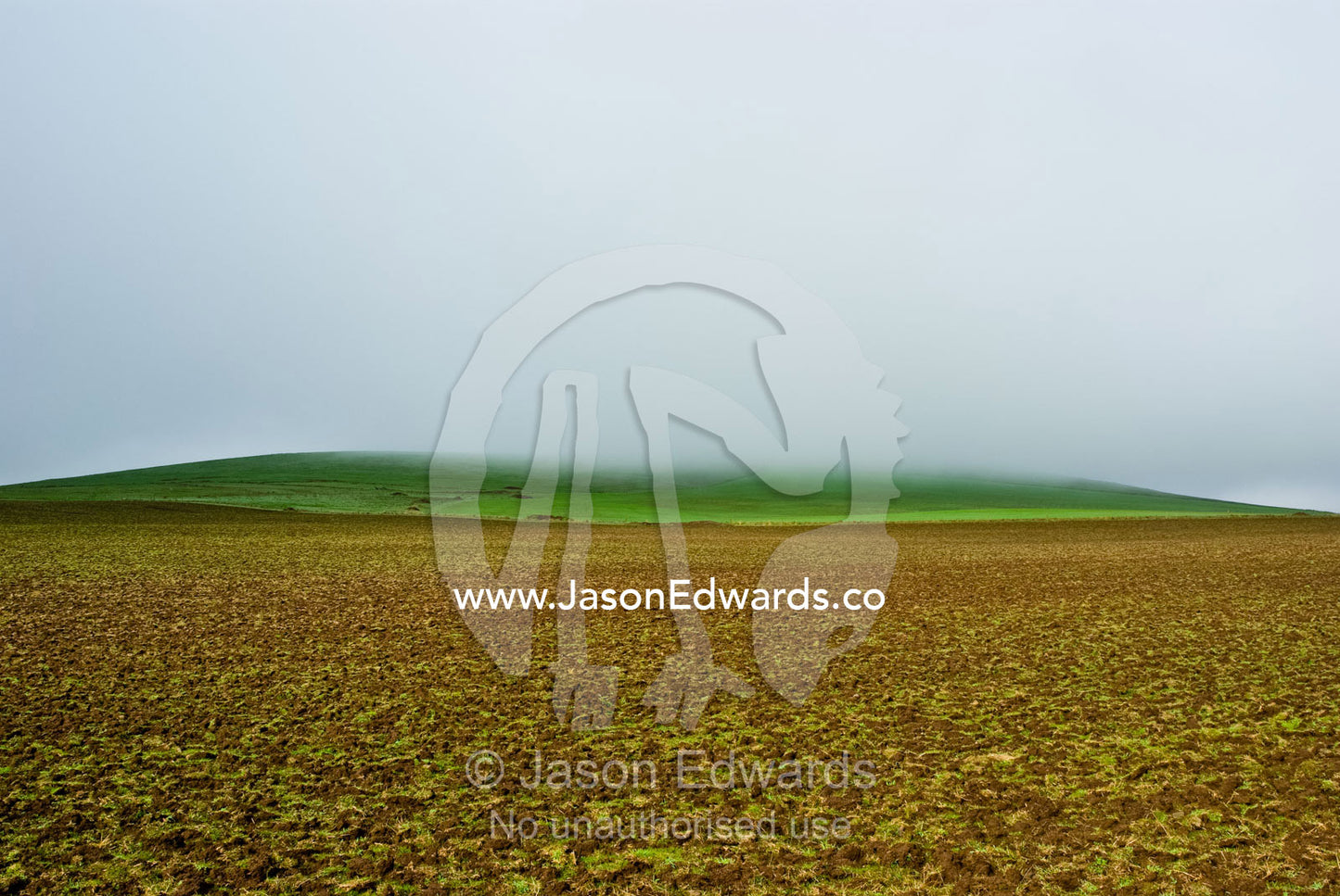 Mist and rain descend on a small hillock over newly ploughed farmland. near Basalt, Daylesford District, Victoria, Australia.