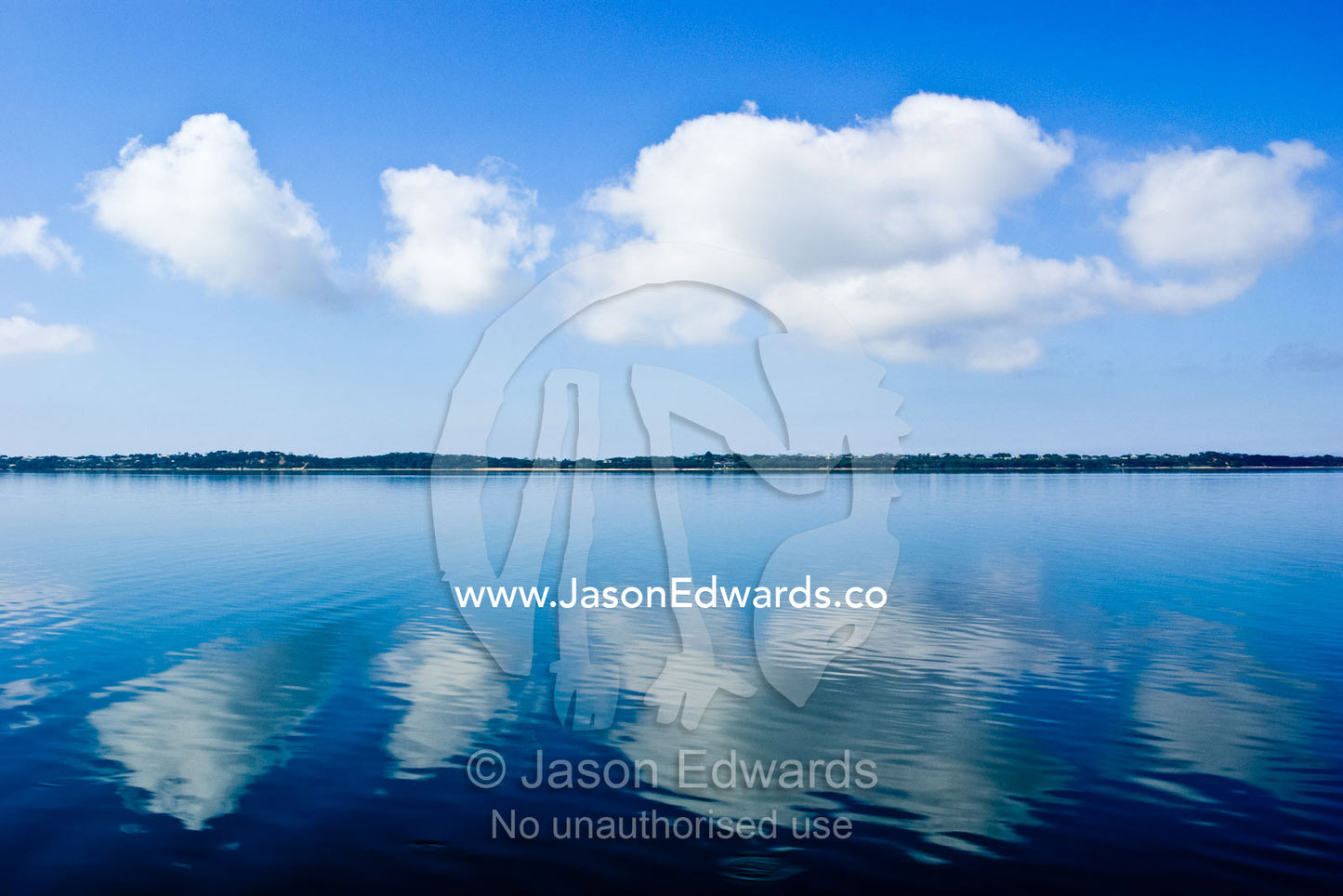 Fluffy clouds float over a perfectly still lake on a hot summers day. Gippsland Lakes Coastal Park, Victoria, Australia.
