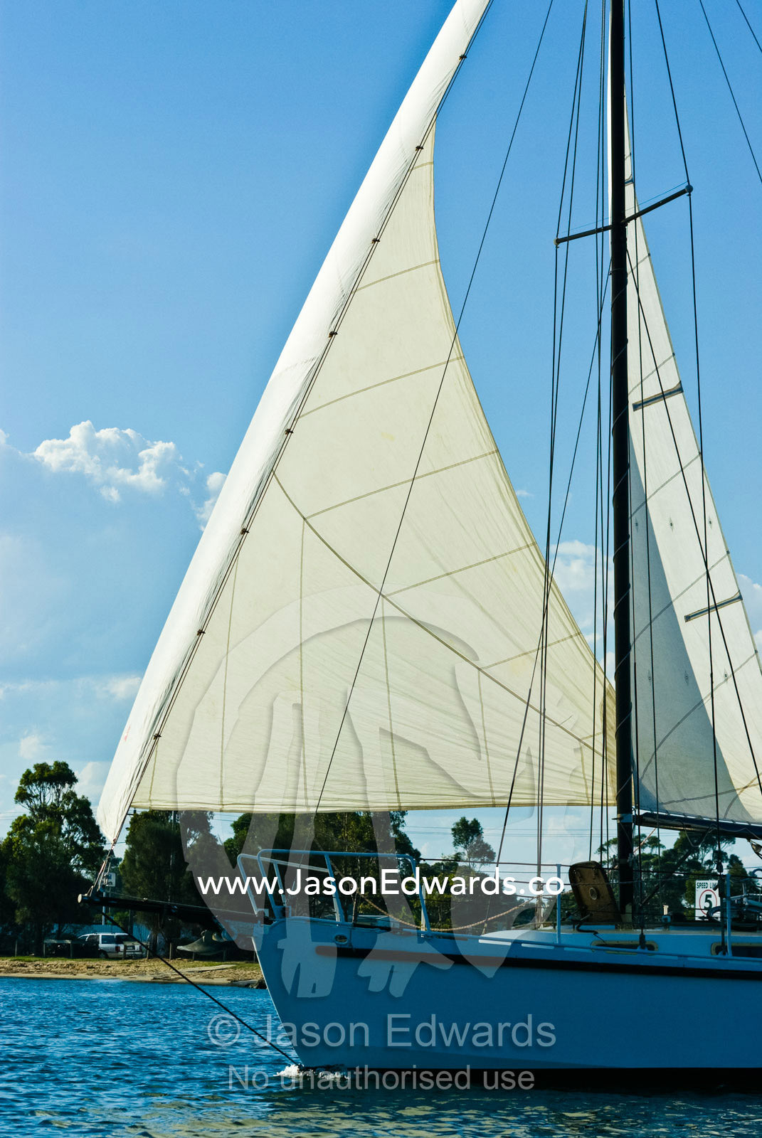 A yacht under full sail glides into a sheltered bay on a summers day. Bancroft Bay, Victoria, Australia.