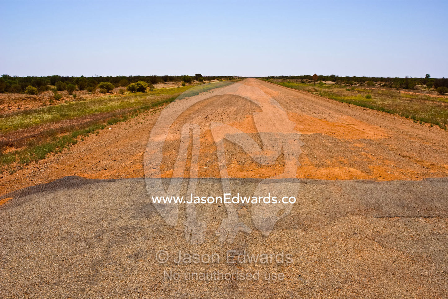 A bitumen road becomes a dirt track heading across the desert plain. Outback western New South Wales, Australia.