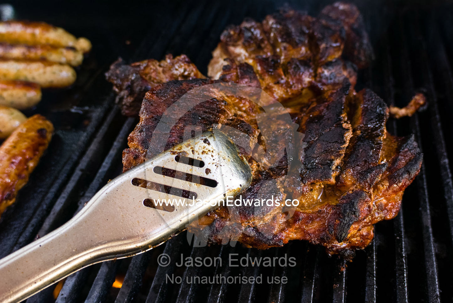 Stainless steel tongs flip a steak whilst sizzling on a barbeque grill Mount Martha, Victoria, Australia.