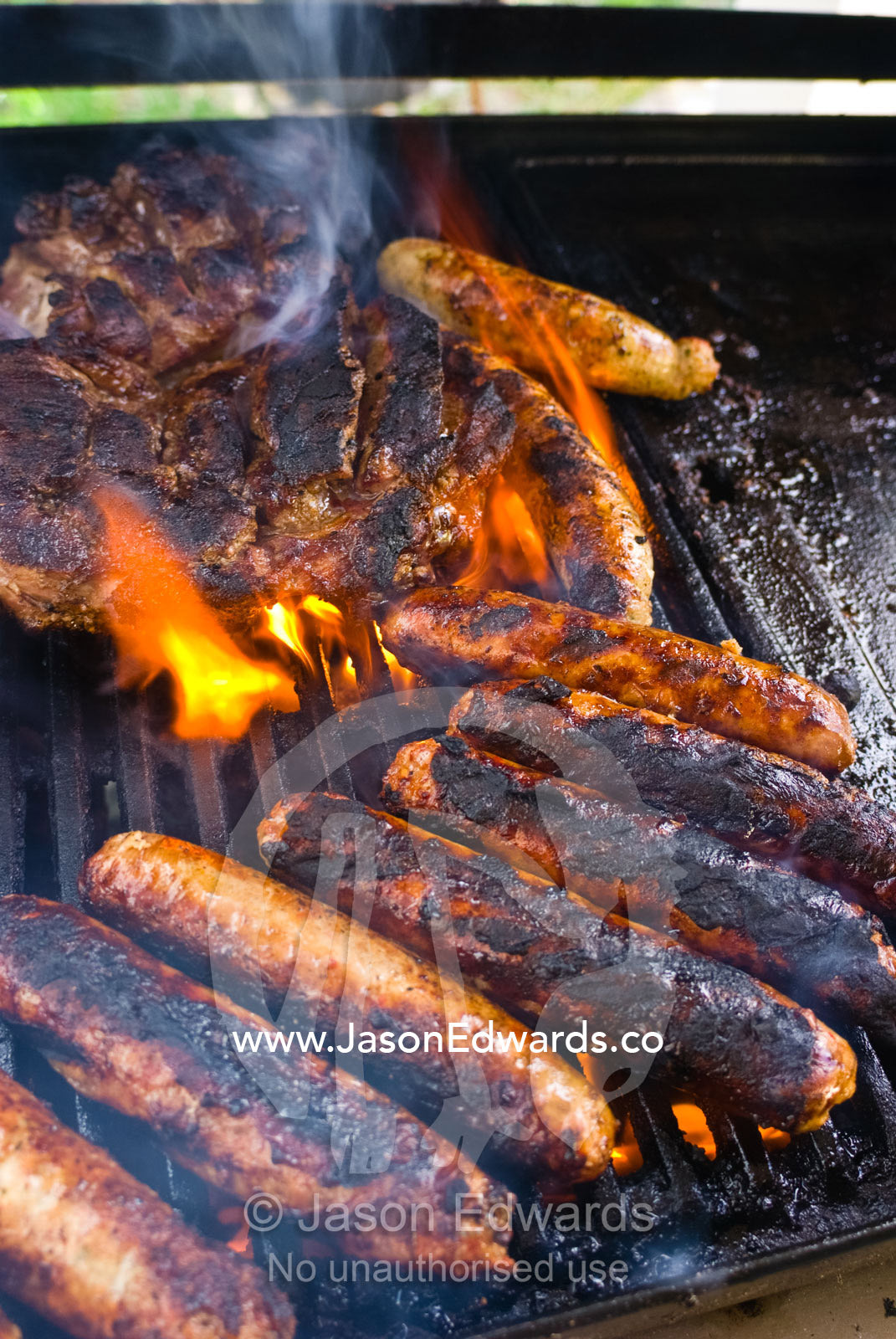 Flame engulfs beef sausages and steak sizzling on a barbeque grill. Mount Martha, Victoria, Australia.
