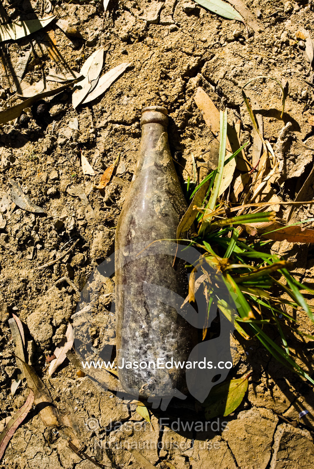An old beer bottle lies in dry river mud exposed by the drought. Bullatail Creek, Mundiwa Station, Deniliquin, New South Wales, Australia.