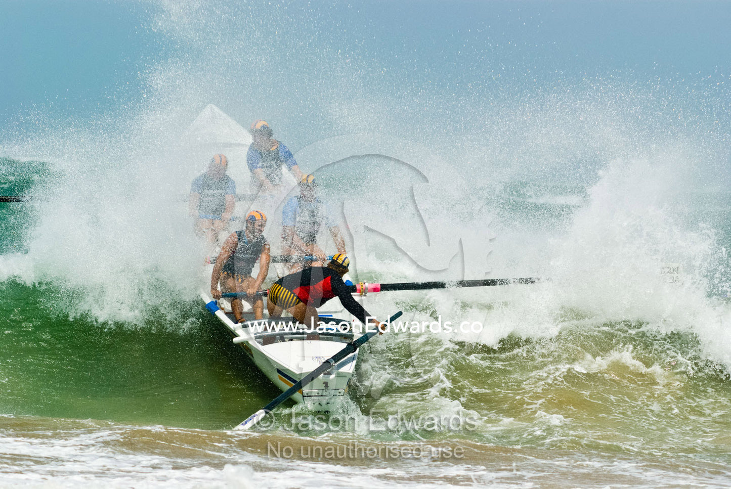 A surf boat crests the top of a green wave in rough seas in a race. Australian Surfboat Open Titles, Fishermen's Bay, Torquay, Victoria, Australia.