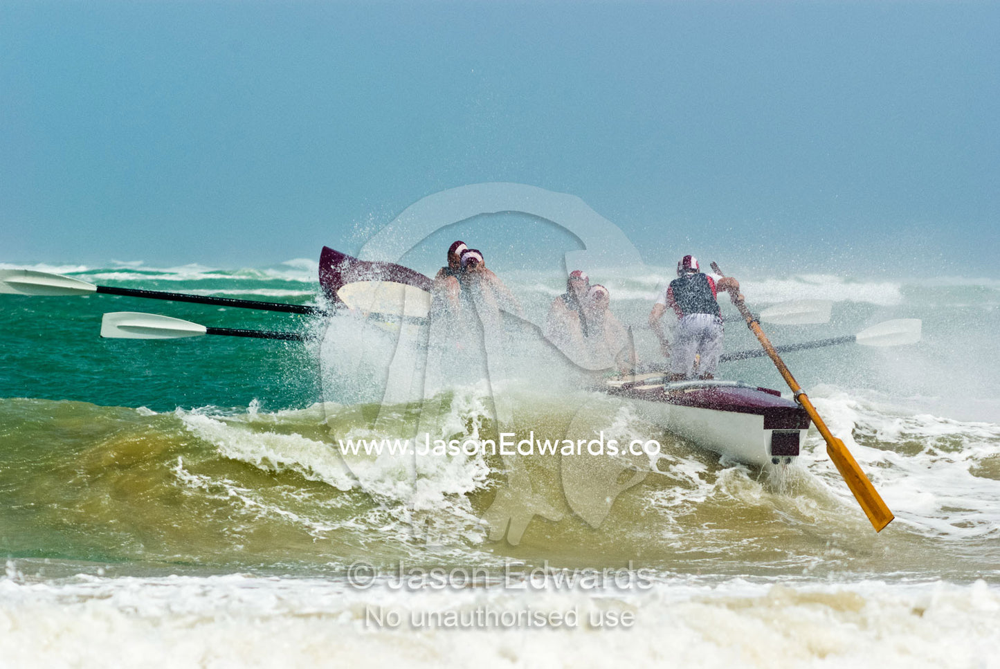 A surf boat crests the top of a green wave in rough seas in a race. Australian Surfboat Open Titles, Fishermen's Bay, Torquay, Victoria, Australia.