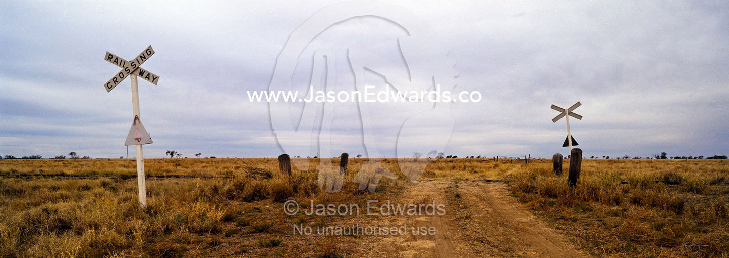 A track crosses a remote outback railway line on a featureless plain. Kennedy Developmental Road, near Hughenden, Queensland, Australia