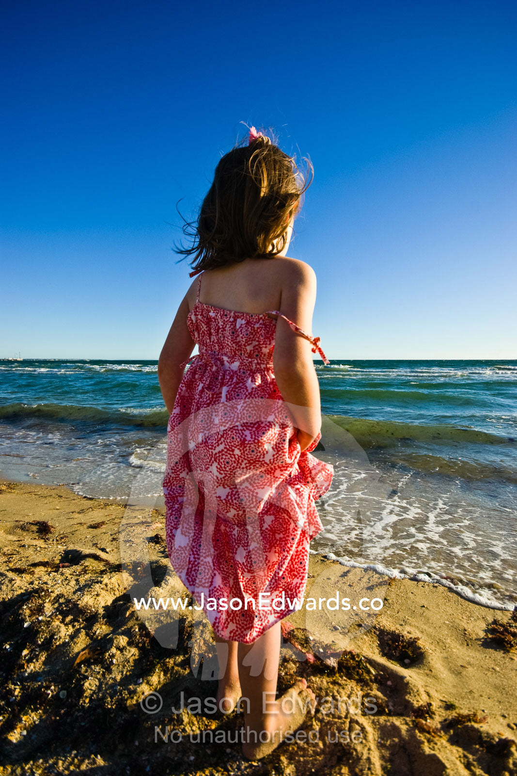 A young girl stands before a windswept ocean on a bright summer day. Port Melbourne Beach, Victoria, Australia.