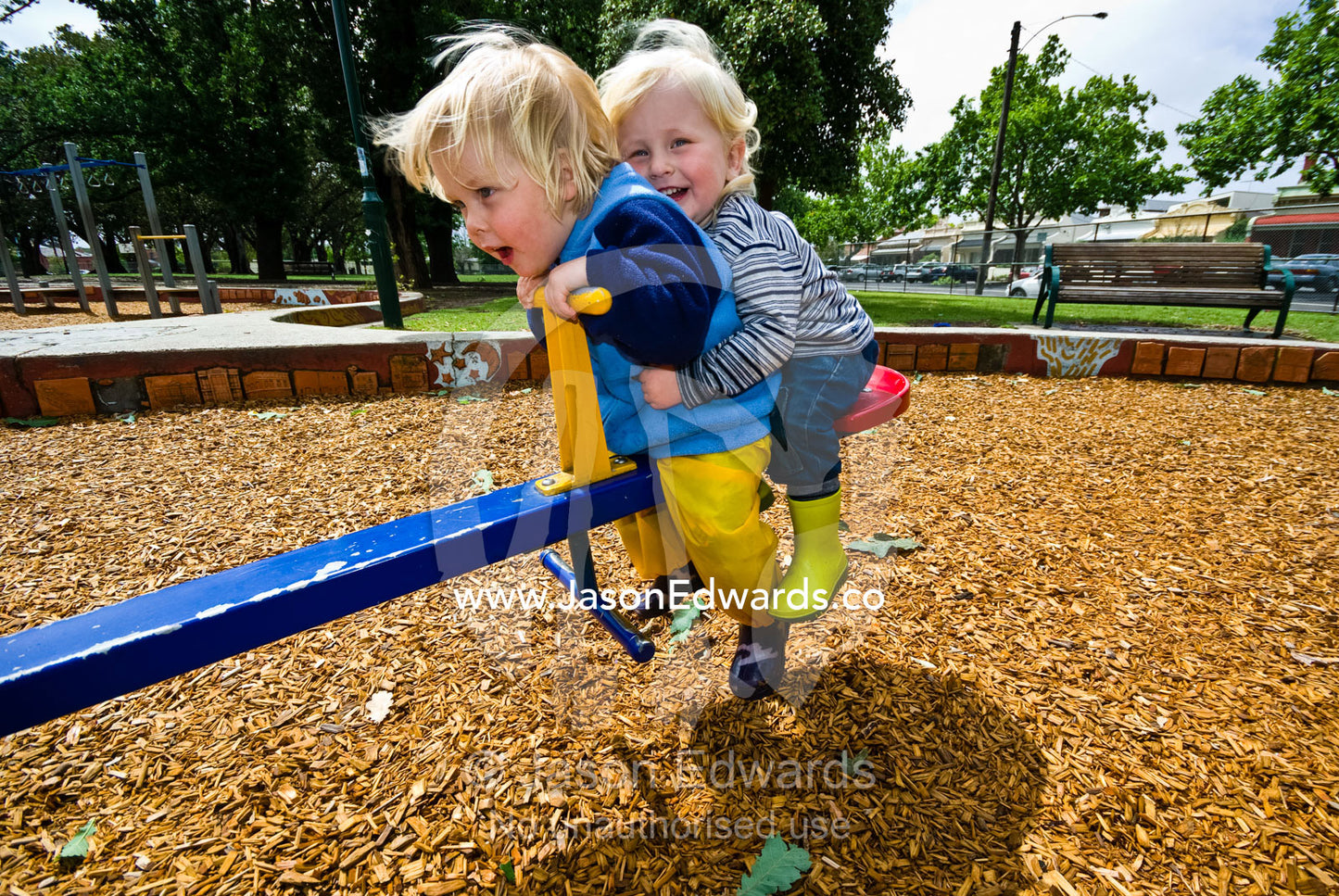 Two young friends enjoy a ride on a seesaw in a community playground. Curtain Square, Carlton North, Victoria, Australia.