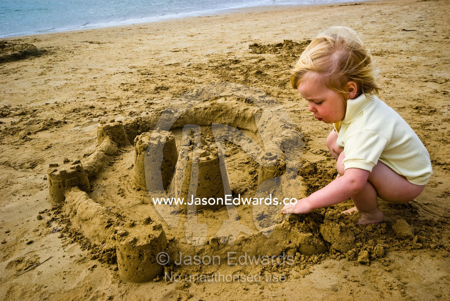 A toddler concentrates while building a sand castle on a beach. Barwon Heads, Bellarine Peninsula, Victoria, Australia.