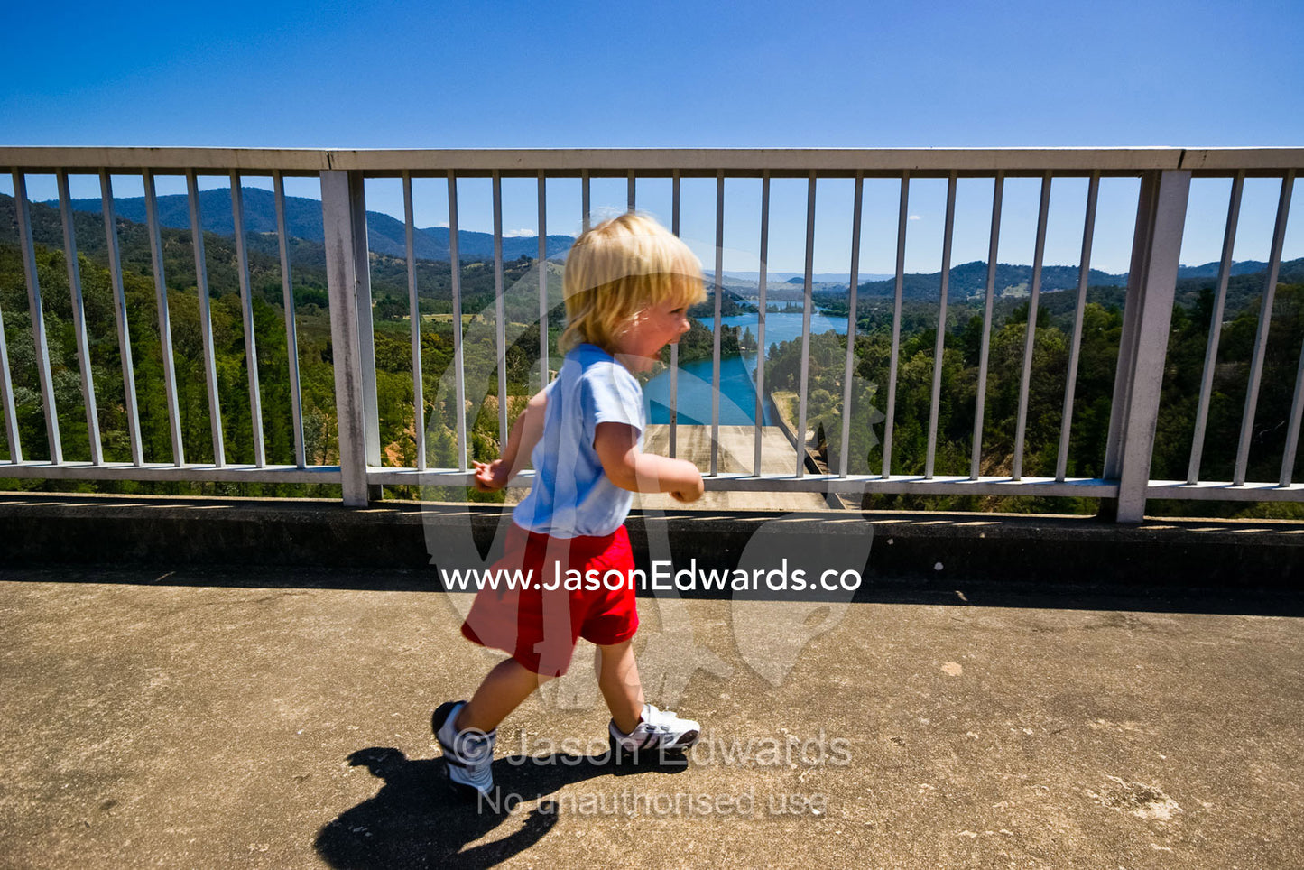 A toddler runs across the top of a dam wall on a sunny summers day. Eildon Weir Spillway, Lake Eildon, Victoria, Australia