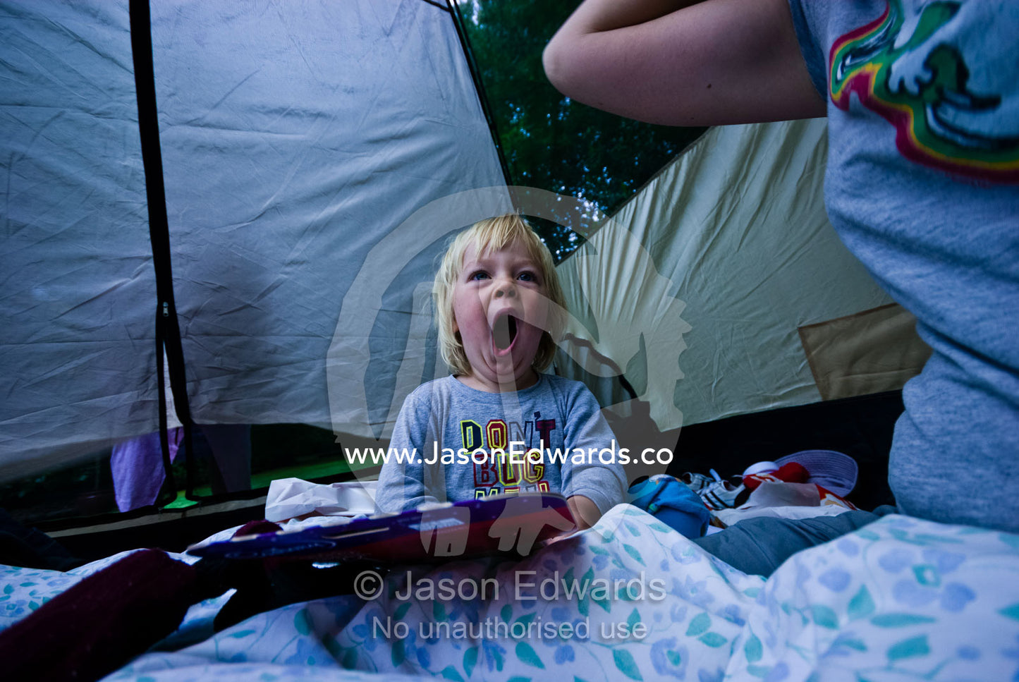 A young boy yawns widely after waking-up in a tent whilst camping. Jamieson, Victoria, Australia