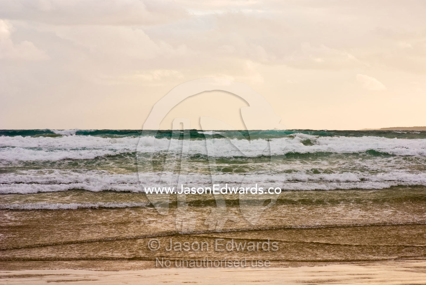 Storm clouds reflect pastel colors in rough waves rolling into shore. Waratah Bay, Victoria, Australia.