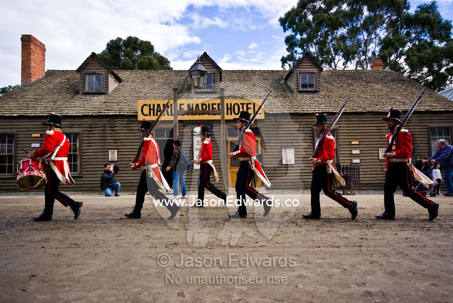 A patrol of British Redcoat soldiers march in formation past a hotel. Ballarat, Victoria, Australia.