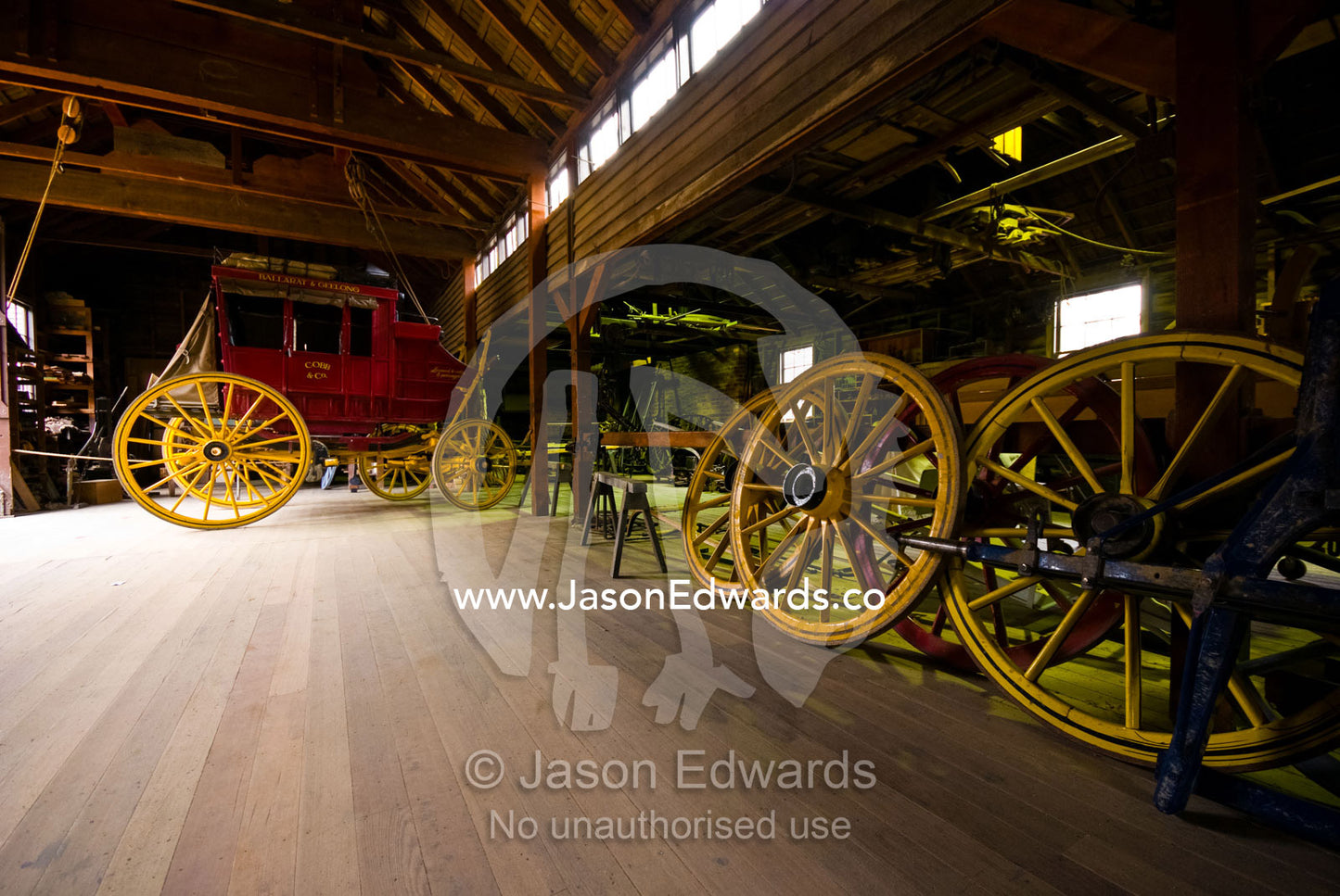 A stagecoach and wagon-wheels await repair in a maintenance workshop. Ballarat, Victoria, Australia.